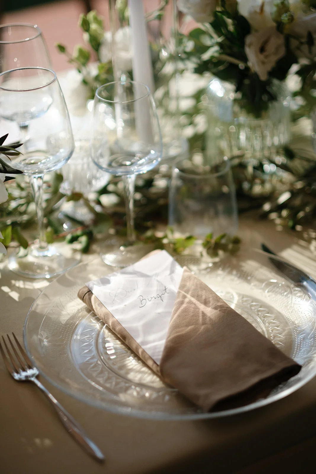 Mise en place di matrimonio con piatto in vetro lavorato, tovagliolo in lino e segnaposto scritto a mano