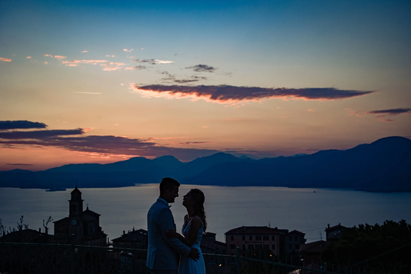Sposi in controluce al tramonto sul Lago di Garda con il campanile di Albisano