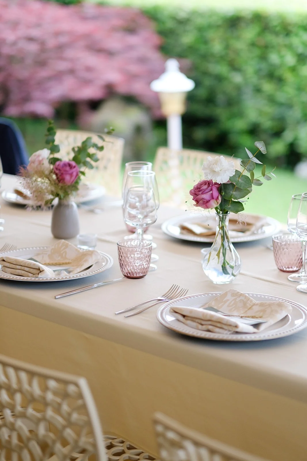 Tavolo apparecchiato in giardino con rose rosa, eucalipto e bicchieri rosati